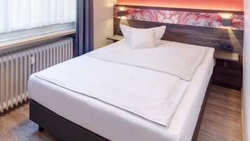 Habitación de hotel con una cama grande, un radiador, una ventana con cortinas y una pared de acento roja.