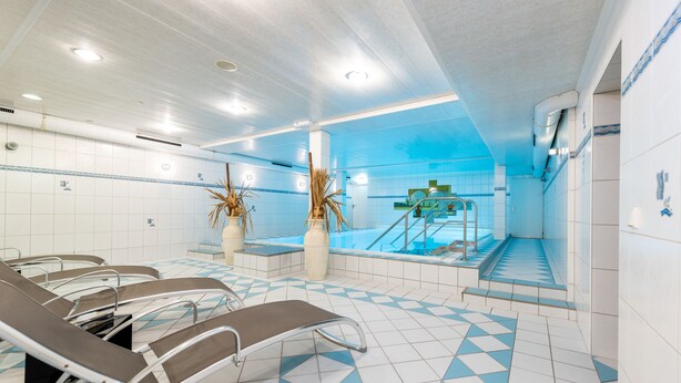 Un área de piscina con sillones de descanso, una escalera y suelo de baldosas.
