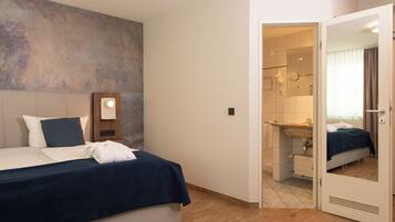 Een hotelkamer met een bed, nachtkastje, spiegel en een zichtbare badkamer door een geopende deur.