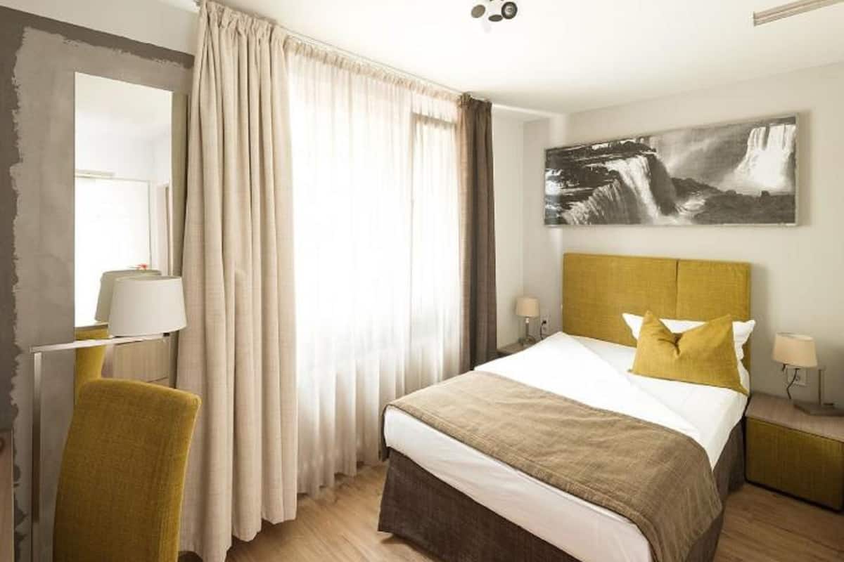 Ein Hotelzimmer mit Bett, Sessel, Schreibtisch, Lampe und einem Bild an der Wand.