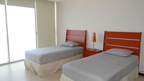 A hotel room with two beds, each with a grey bedspread and white pillows, and a red nightstand with a lamp between them.