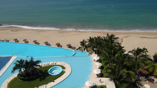 A resort with a large swimming pool, a beach, and palm trees.