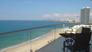 A balcony with a view of a beach and ocean, a chair, and a railing.