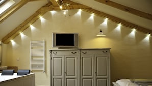 Un dormitorio con cama, televisor en un mueble, radiador y ventana con luces.