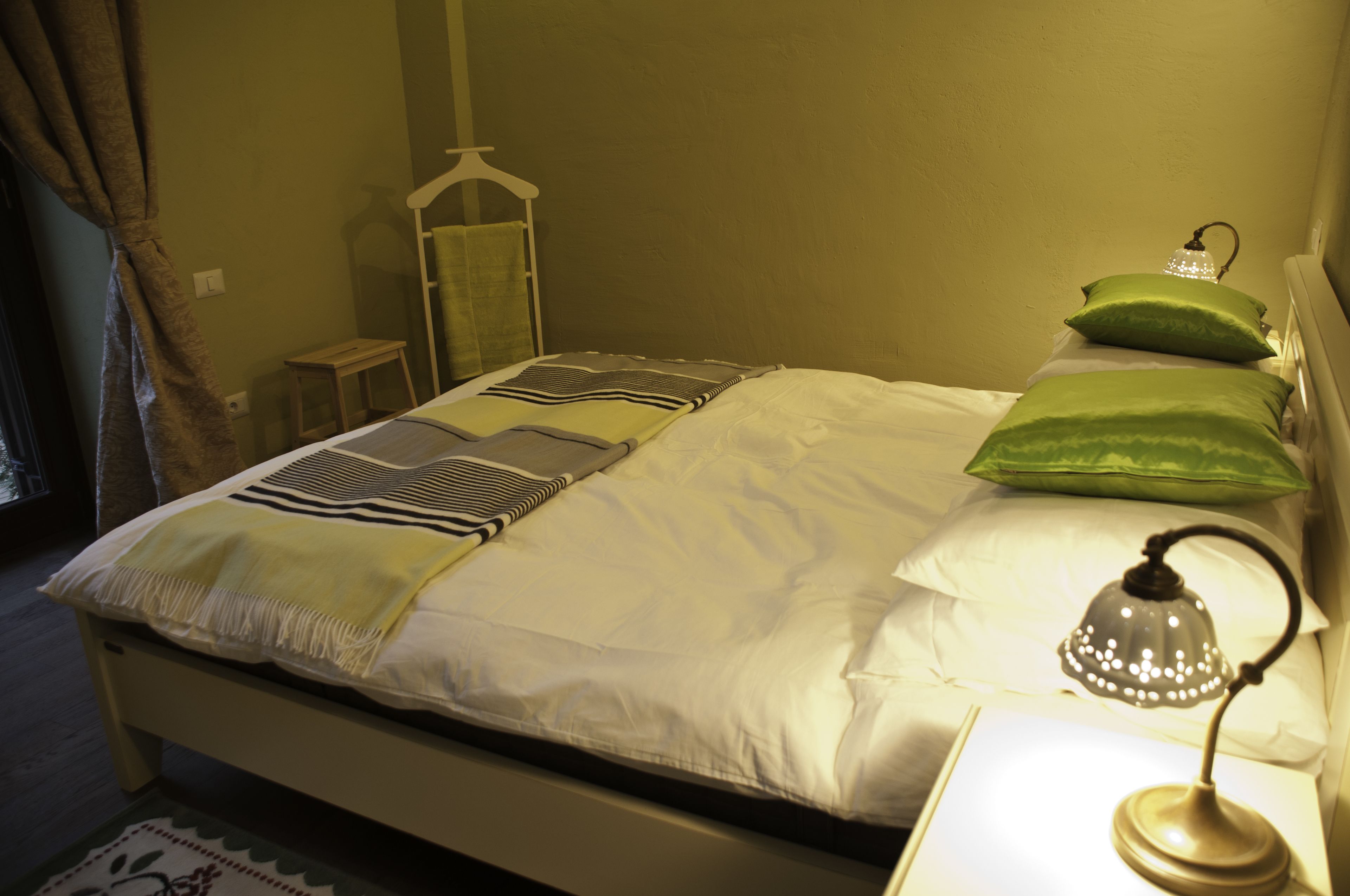 A neatly made bed with a striped blanket and pillows, a bedside table with a lamp, and a small stool.