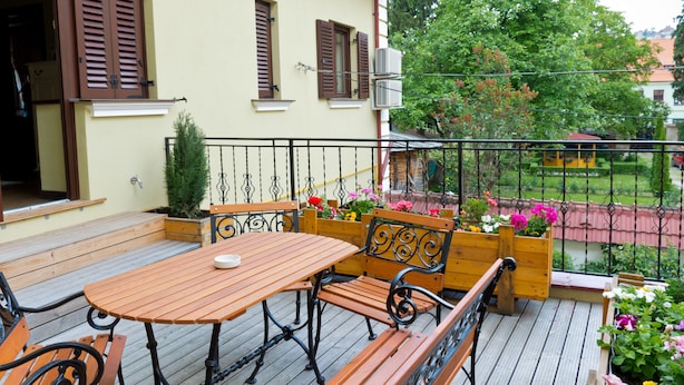 Una terraza de madera con una mesa y bancos, rodeada de plantas y flores en macetas.
