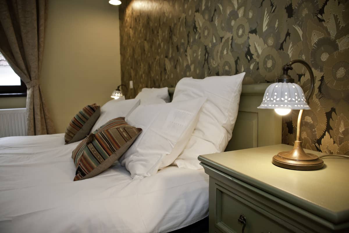 A neatly made bed with white linens and striped pillows, a bedside lamp, and a patterned wallpaper.