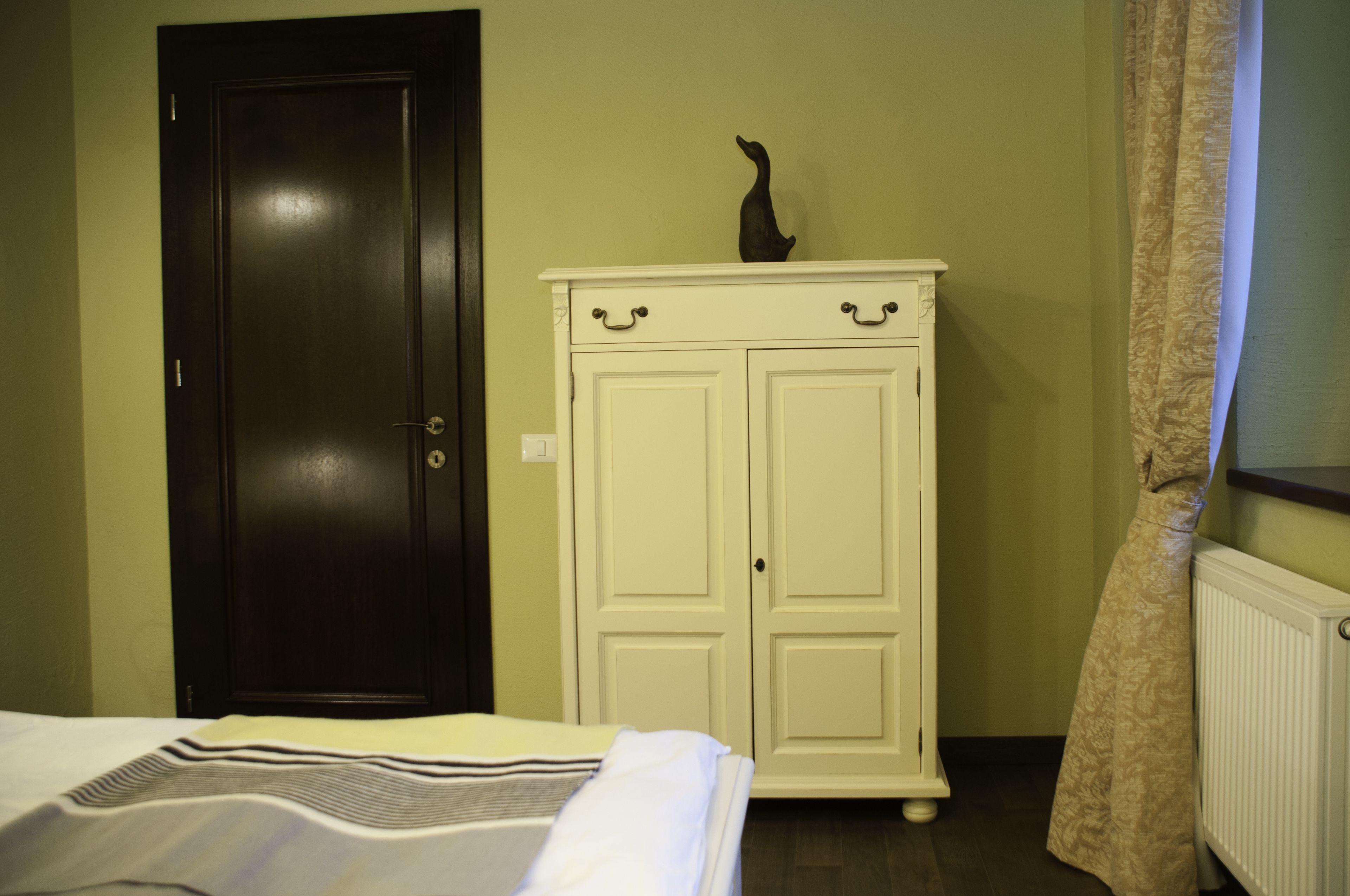 Une pièce avec un lit, une armoire blanche, une porte sombre et un radiateur.