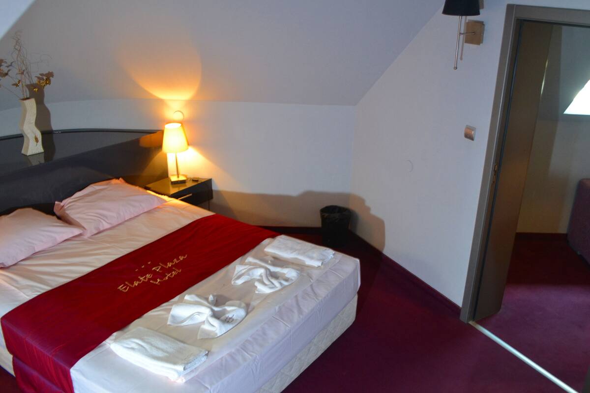 Ein Hotelzimmer mit einem Bett, einem Nachttisch, einer Lampe, einem an der Wand montierten Telefon und einer Tür zu einem anderen Raum.