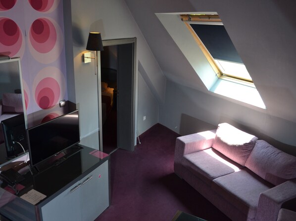 A compact room with a desk, a couch, and a skylight.