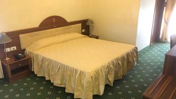 A hotel room with a bed, a bedside table with a lamp, a telephone, and a green patterned carpet.