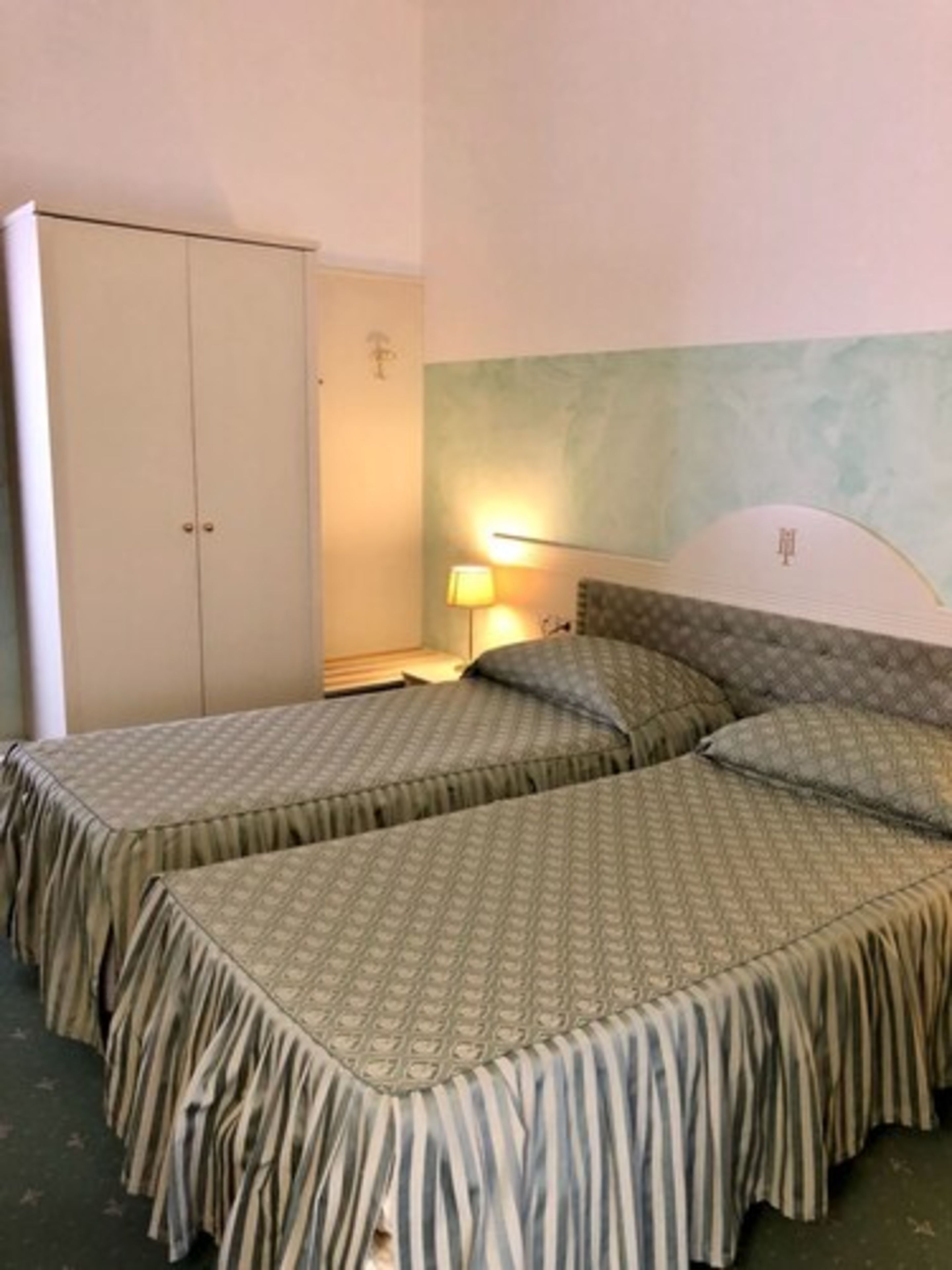 A room with two beds, a wardrobe, a nightstand, and a lamp.