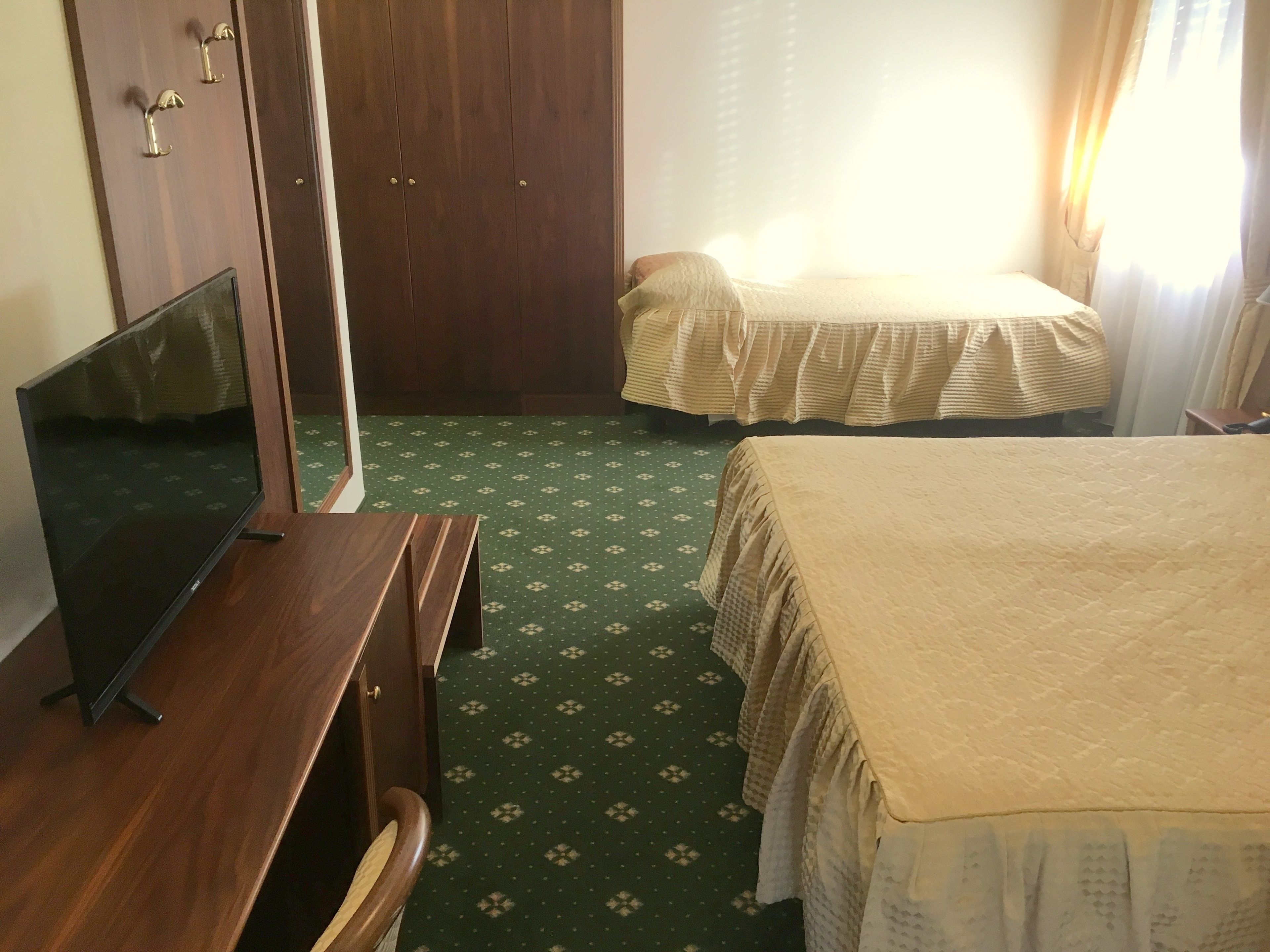 A hotel room with two beds, a wooden desk, a television, and a wardrobe.