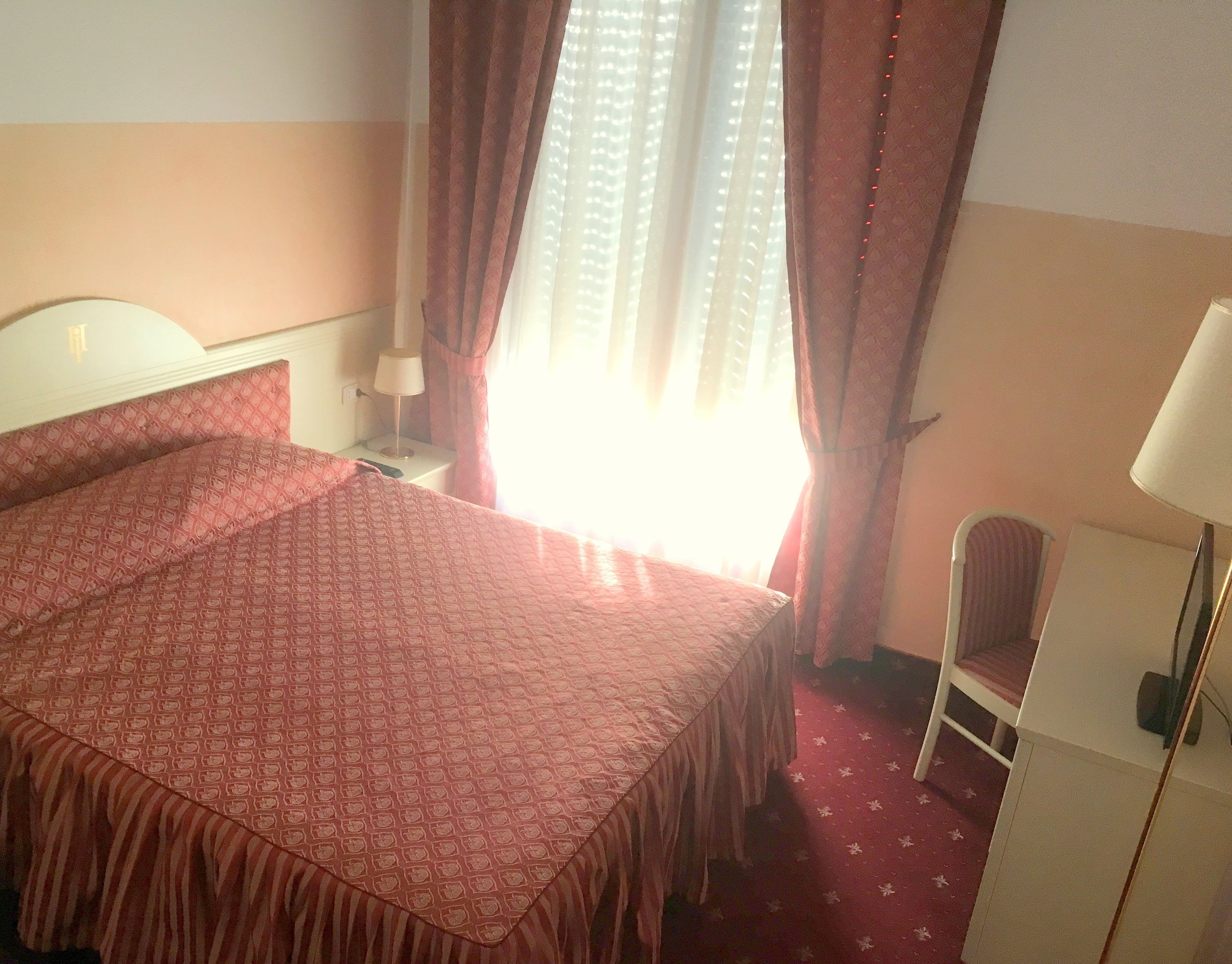A hotel room with a bed, a nightstand, a lamp, a chair, and a window with curtains.