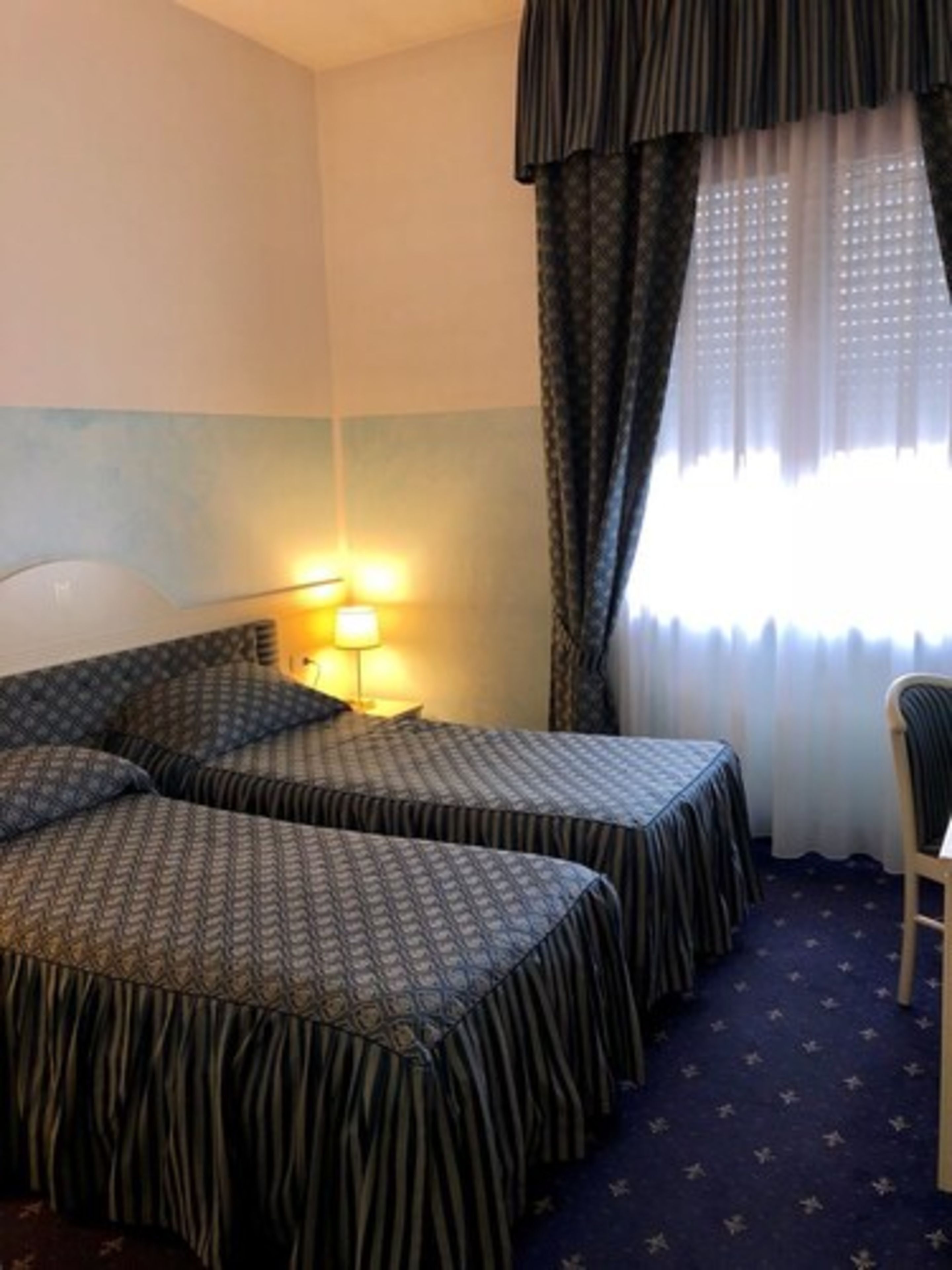 Ein Hotelzimmer mit zwei Betten, einem Nachttisch, einer Lampe und einem Stuhl.