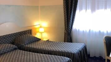 Habitación de hotel con dos camas, una mesita de noche, una lámpara y una silla.