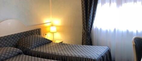 Habitación de hotel con dos camas, una mesita de noche, una lámpara y una silla.