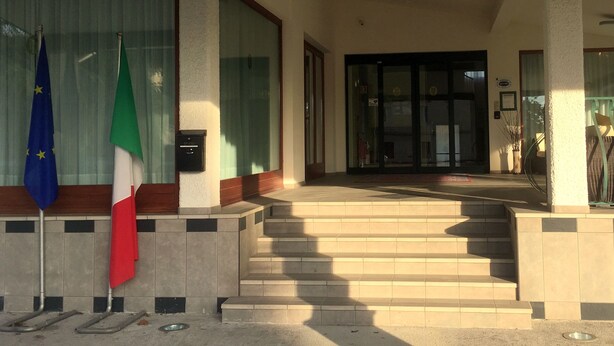 A hotel entrance with a set of stairs leading to a door, a mailbox, and two flags on poles. - Hotel Internazionale (Gorizia)