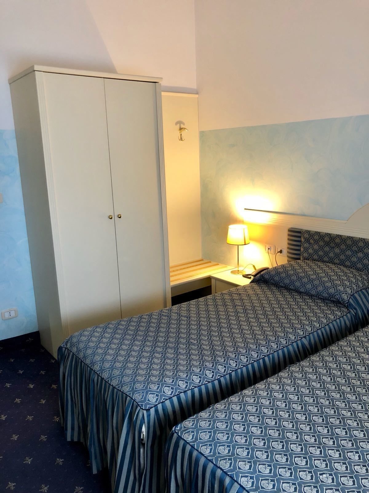 Une chambre d’hôtel comprenant un lit, une armoire, une table de chevet avec une lampe et une tête de lit à motifs.