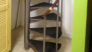A spiral staircase with metal railings and wooden handrails, leading to an upper floor.
