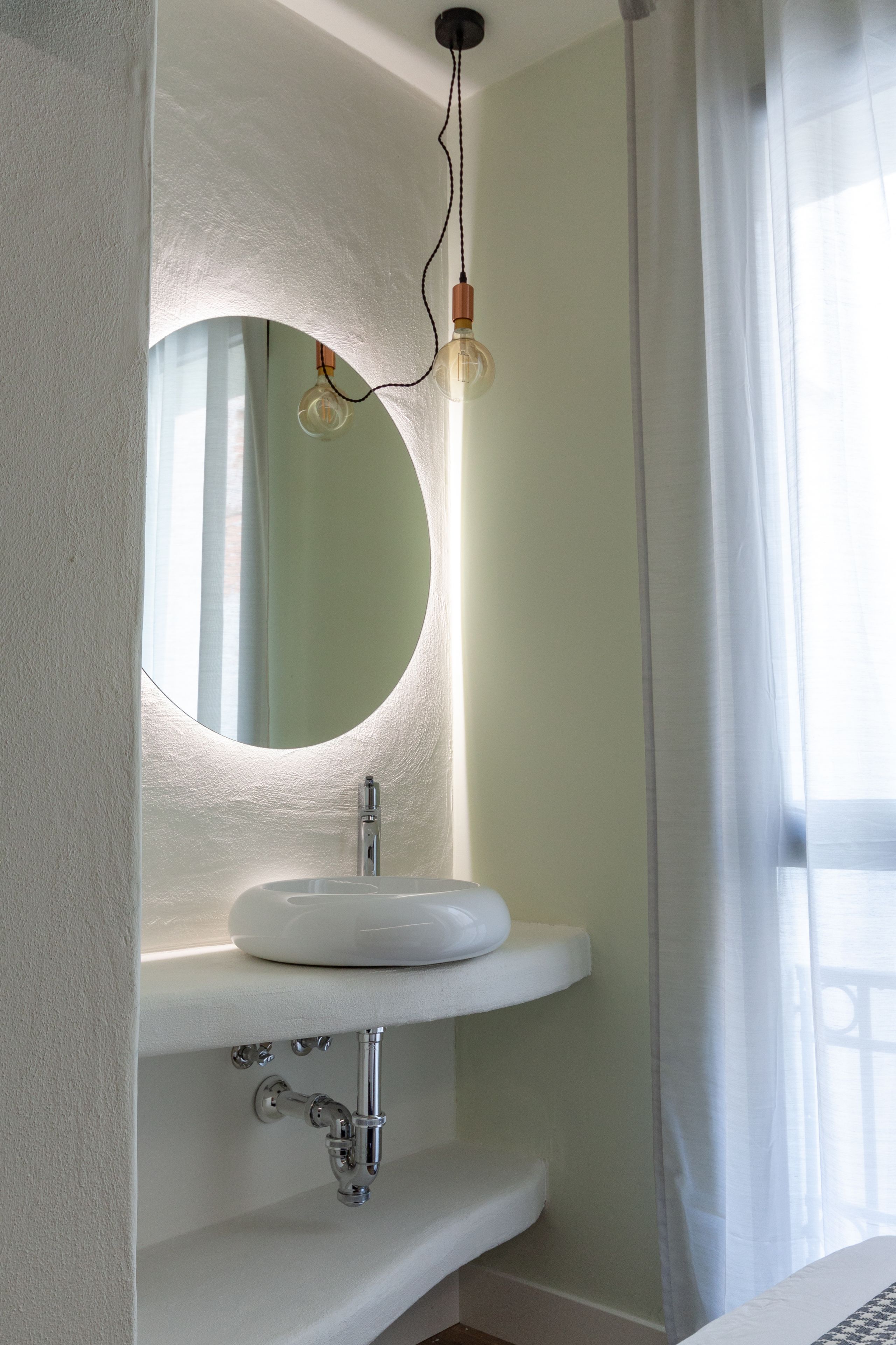 A bathroom with a white sink, a round mirror, and a pendant light.