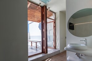 A modern bathroom with a large mirror, a white sink, and a wooden door leading to an outdoor area with a table and chairs. - Hostal Charlotte (Madrid)