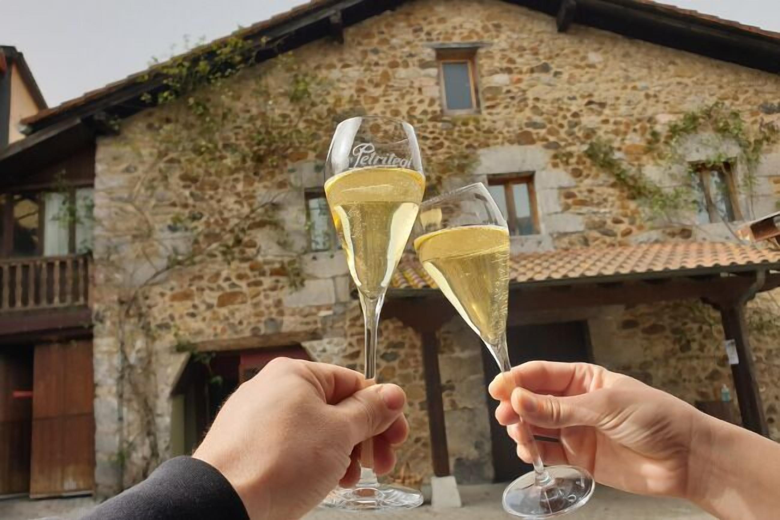 Two hands holding champagne glasses with a stone building in the background.