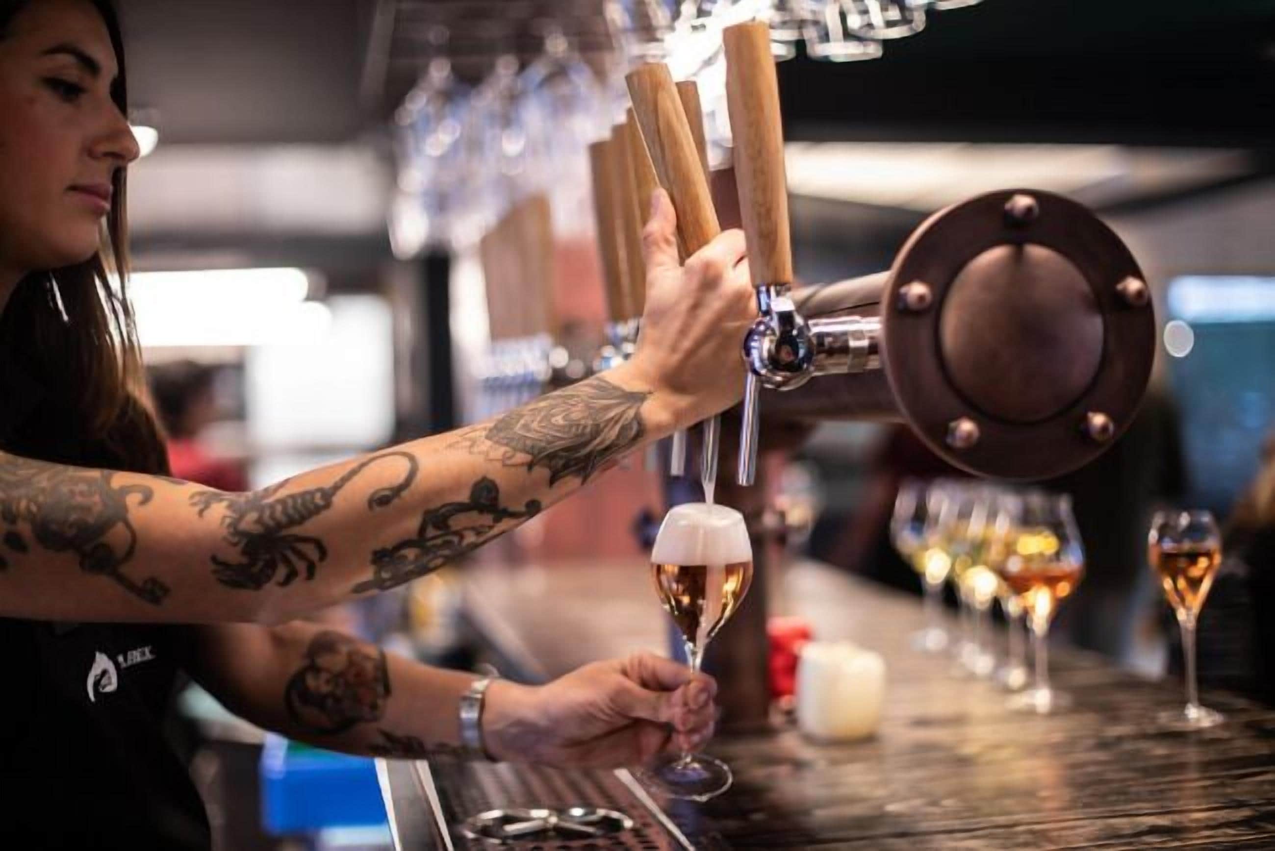 A bartender pouring a drink from a tap into a glass.