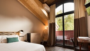 Habitación de hotel con una cama grande, una silla, una mesa y un balcón con vista a árboles.