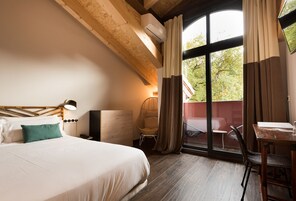 Habitación de hotel con una cama grande, una silla, una mesa y un balcón con vista a árboles.
