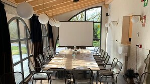 Un salón de conferencias con una larga mesa, sillas, una pizarra blanca y ventanas amplias.