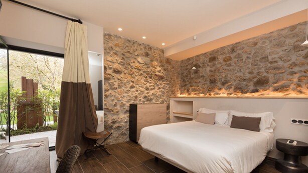Un dormitorio moderno con una pared de acento de piedra, una cama grande, una mesita de noche y vistas al exterior.