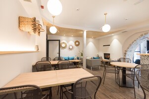 Un área de comedor moderna con mesas y sillas de madera, un sofá y arte decorativo en la pared.