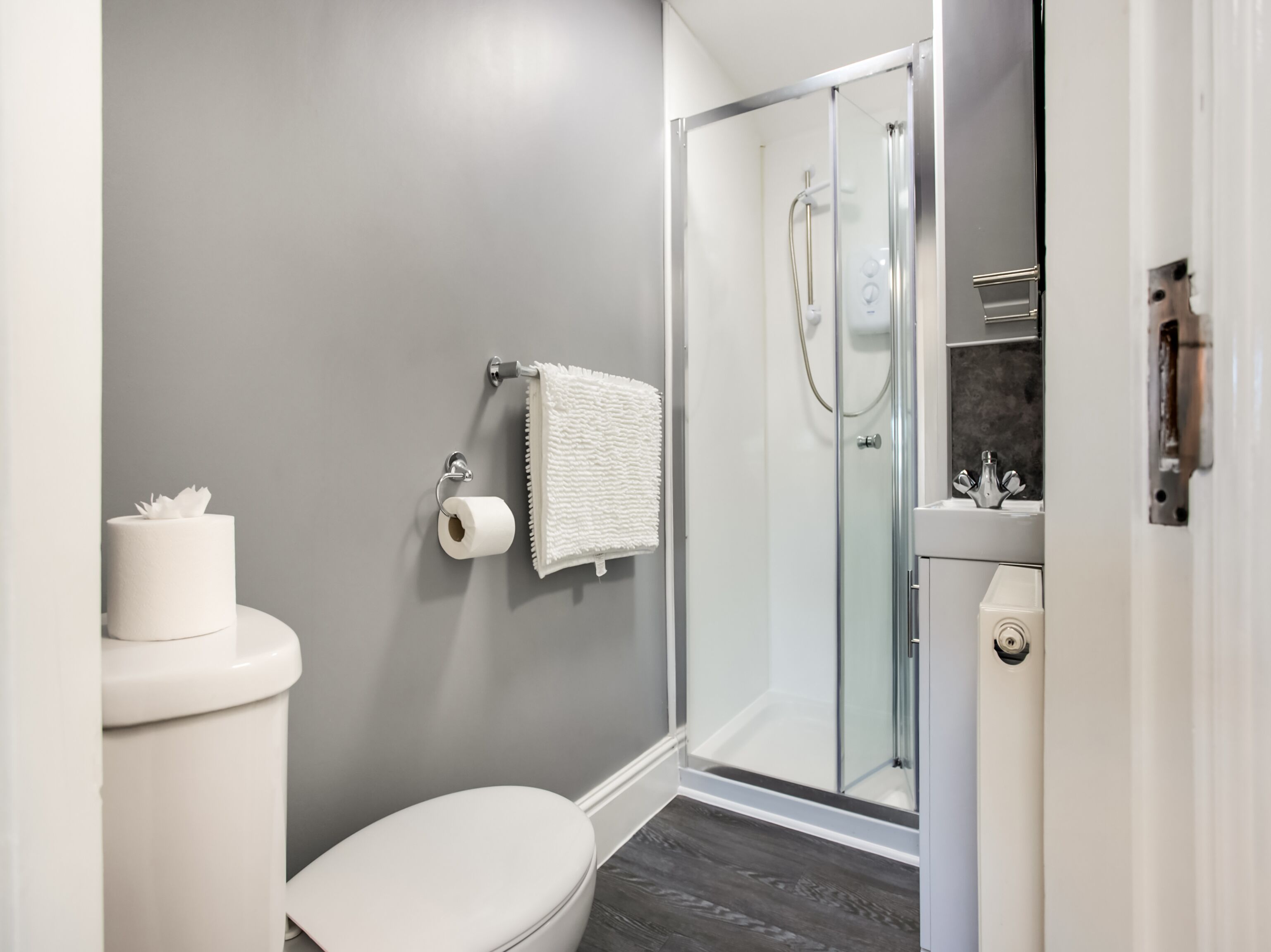 A modern bathroom with a toilet, a shower enclosure, and a towel rack.