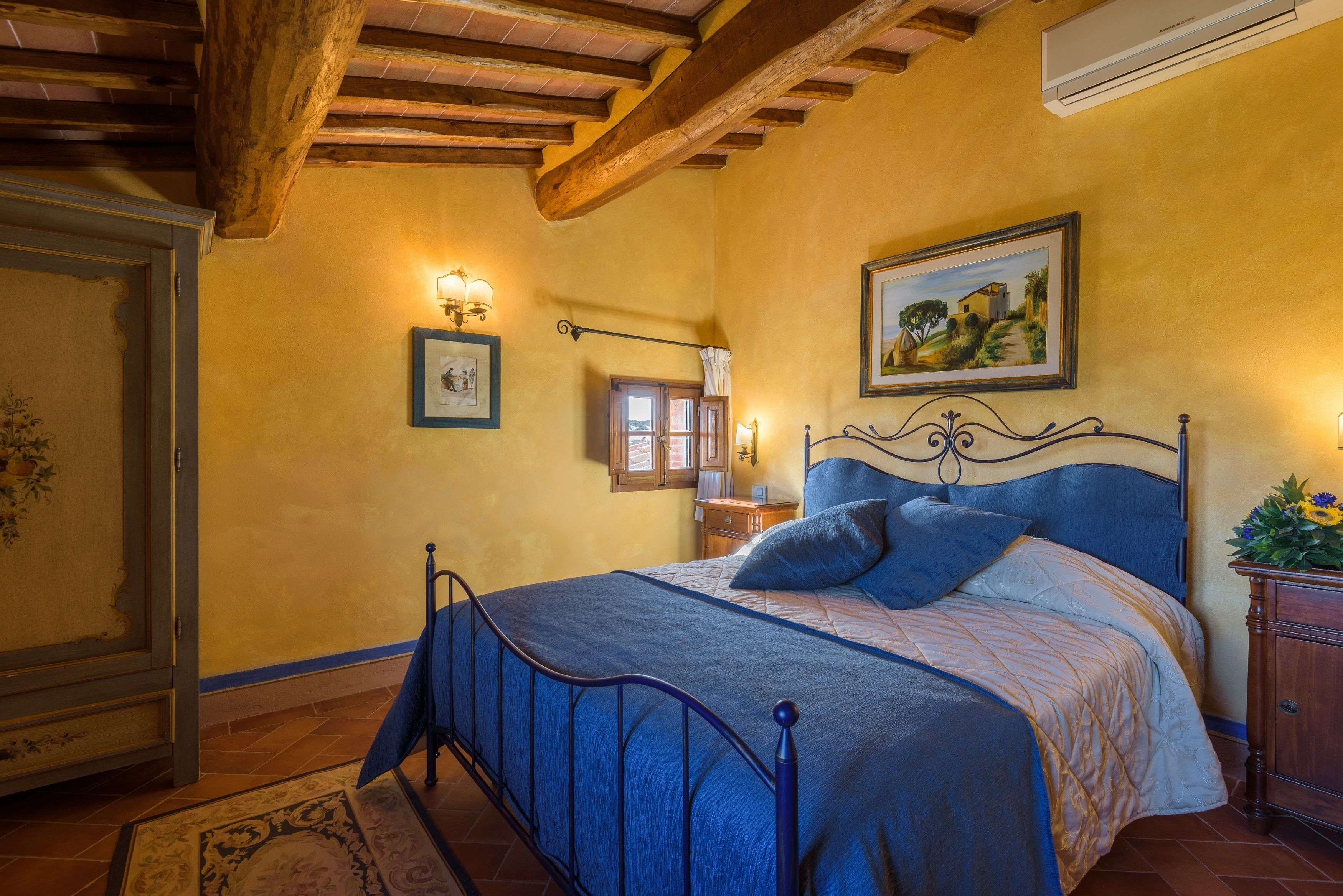 A bedroom with a bed, wooden beams, a painting, and a nightstand.