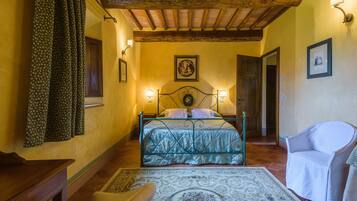 Un dormitorio con cama, una silla, un escritorio y una alfombra estampada.