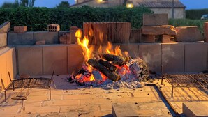 Una chimenea con leña encendida, rodeada de bloques de piedra y una parrilla de metal.