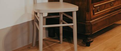 Un aparador de madera con cajones y un espejo, una silla blanca y un suelo de baldosas.