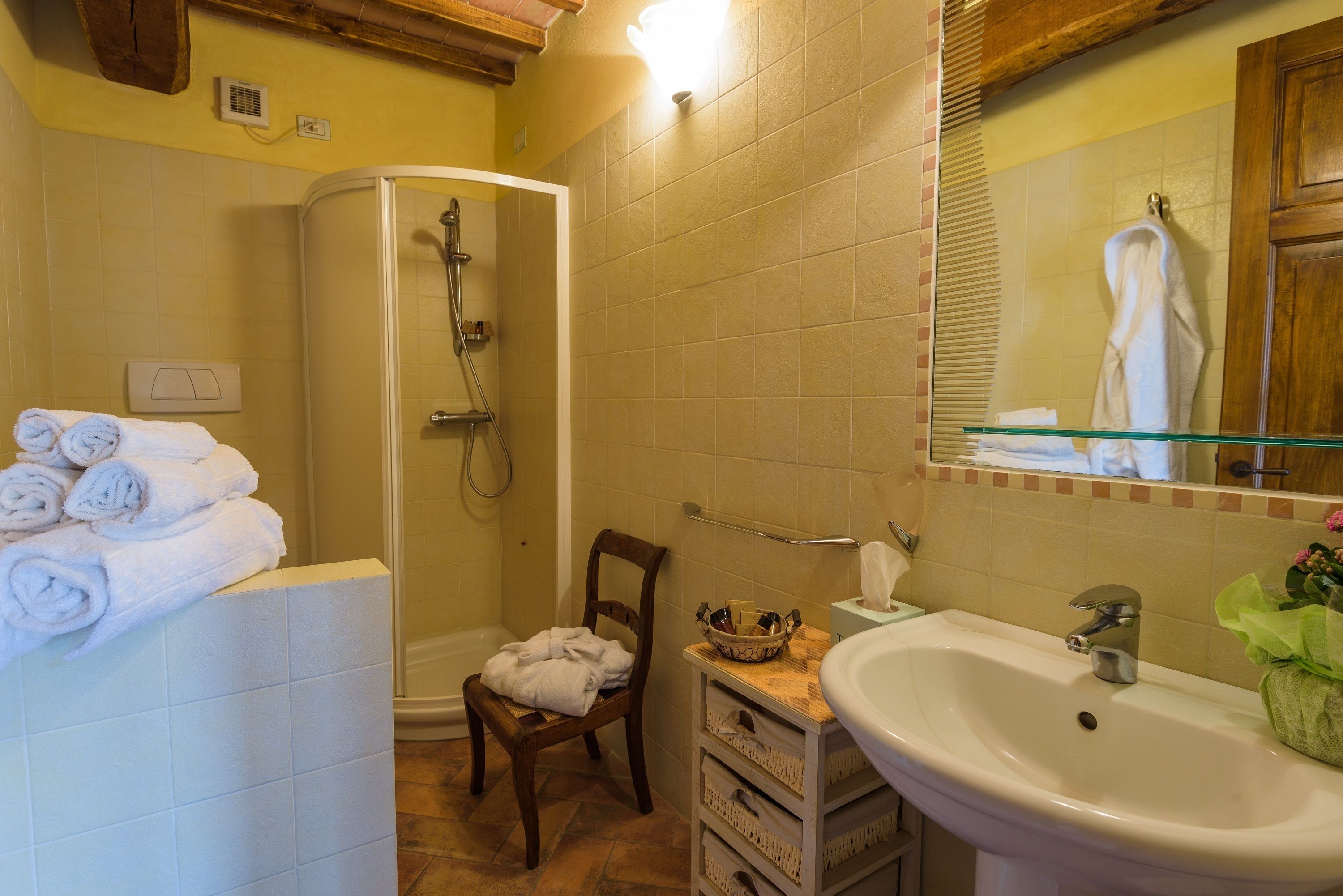 Ein Badezimmer mit Dusche, Waschbecken, Spiegel und einem Sessel.