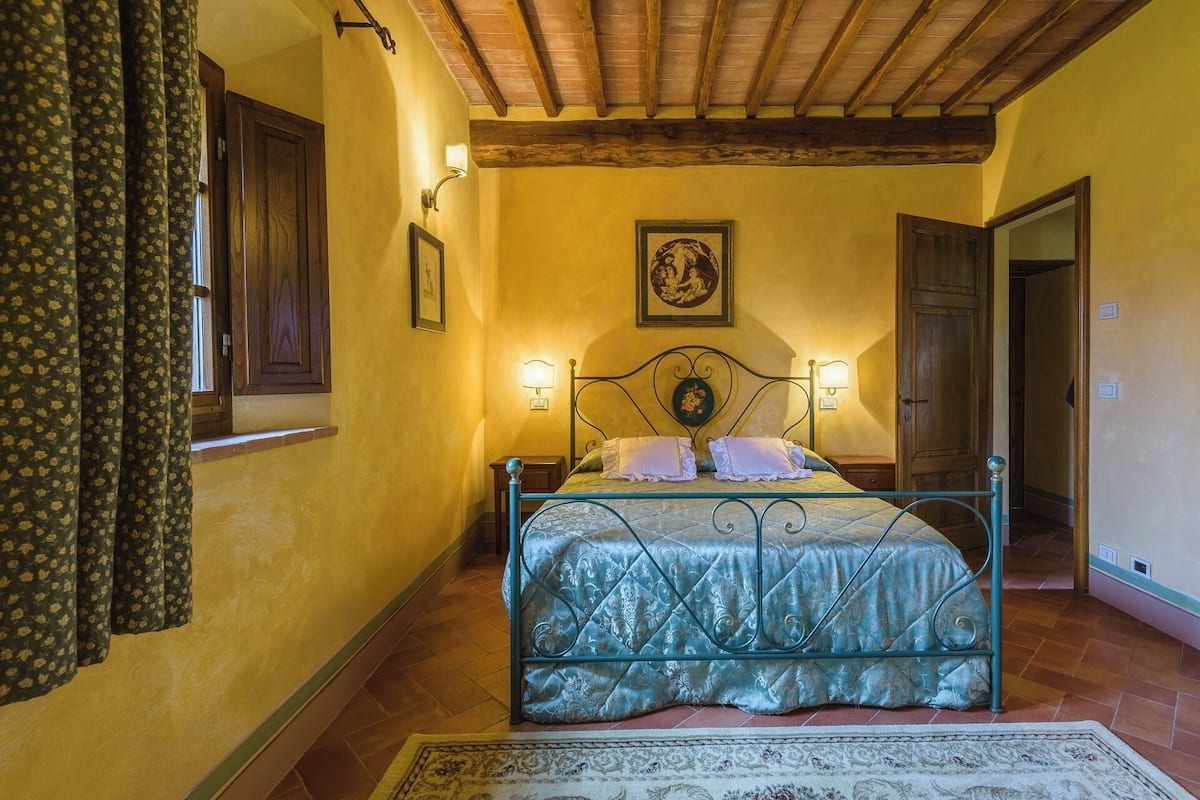 A bedroom with a bed, two bedside lamps, a framed picture on the wall, and a wooden ceiling.