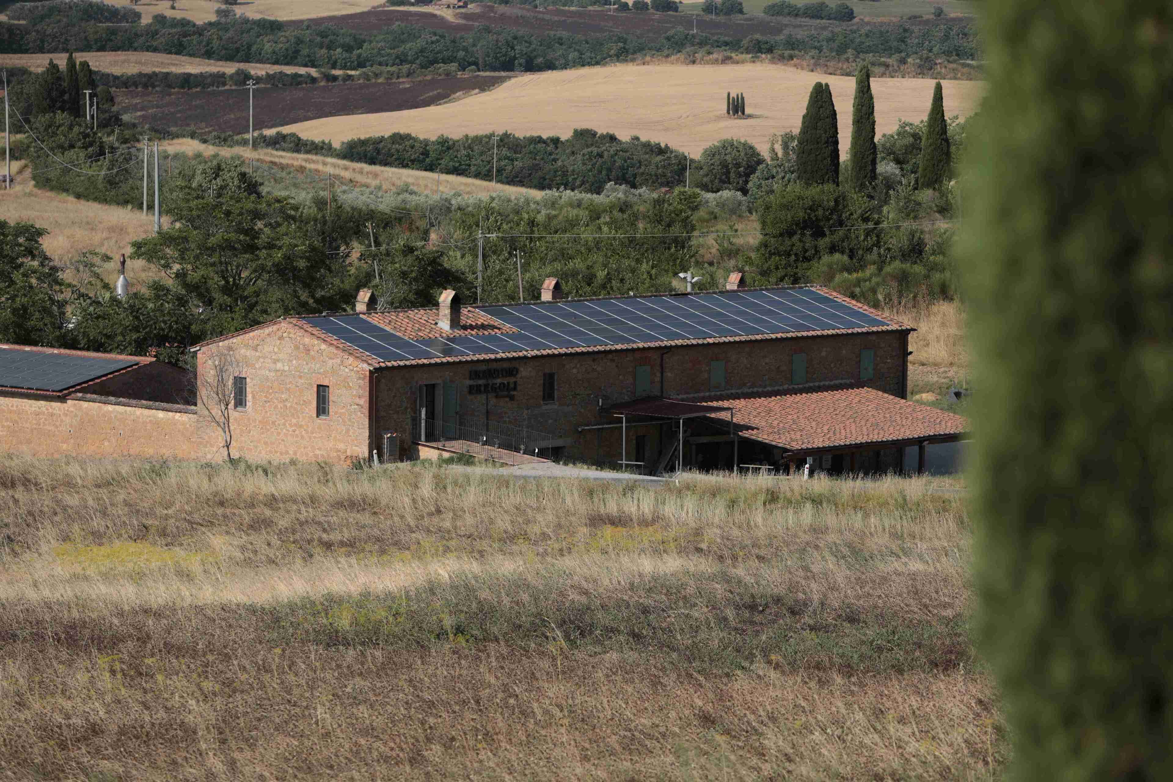 Un edificio rústico con techo inclinado y paneles solares, rodeado de colinas ondulantes y vegetación escasa.