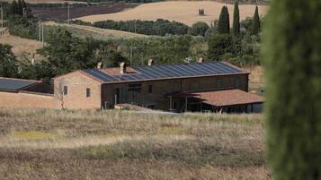 Un edificio rústico con techo inclinado y paneles solares, rodeado de colinas ondulantes y vegetación escasa.