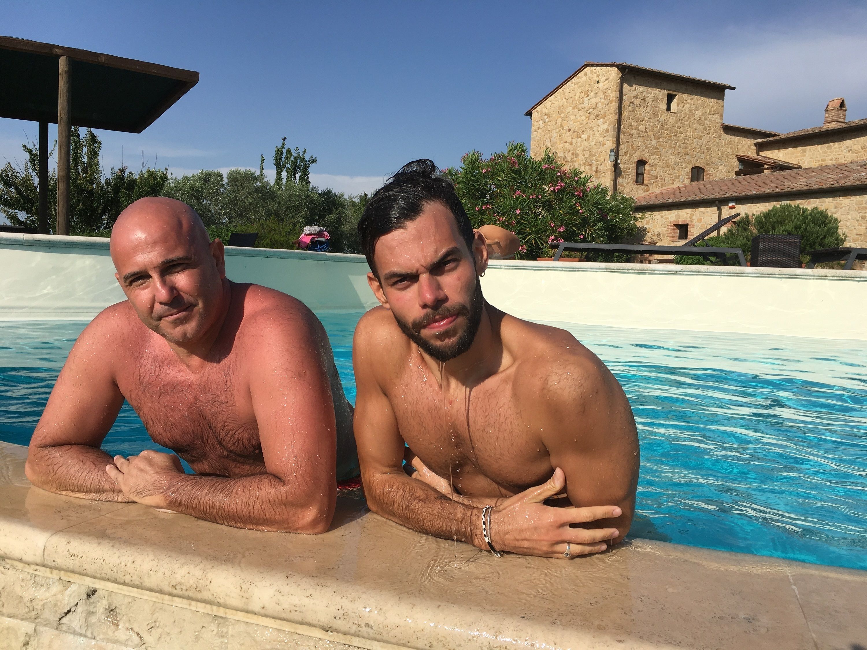 Two men by a pool with stone buildings in the background.