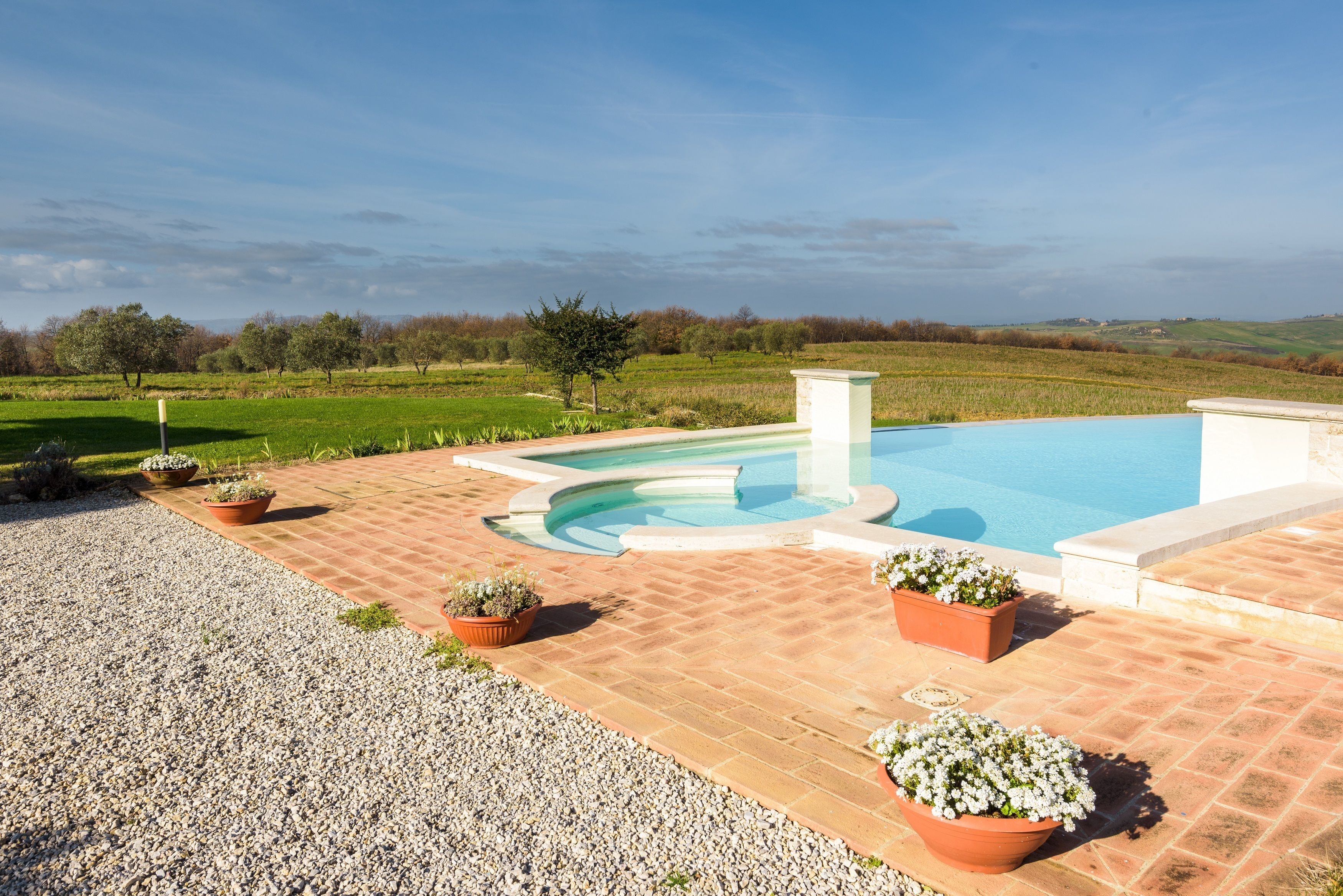 A swimming pool with a curved edge, surrounded by a brick patio, and potted plants.