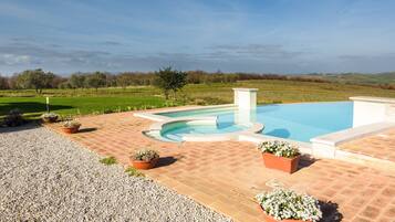 A swimming pool with a curved edge, surrounded by a brick patio, and potted plants.