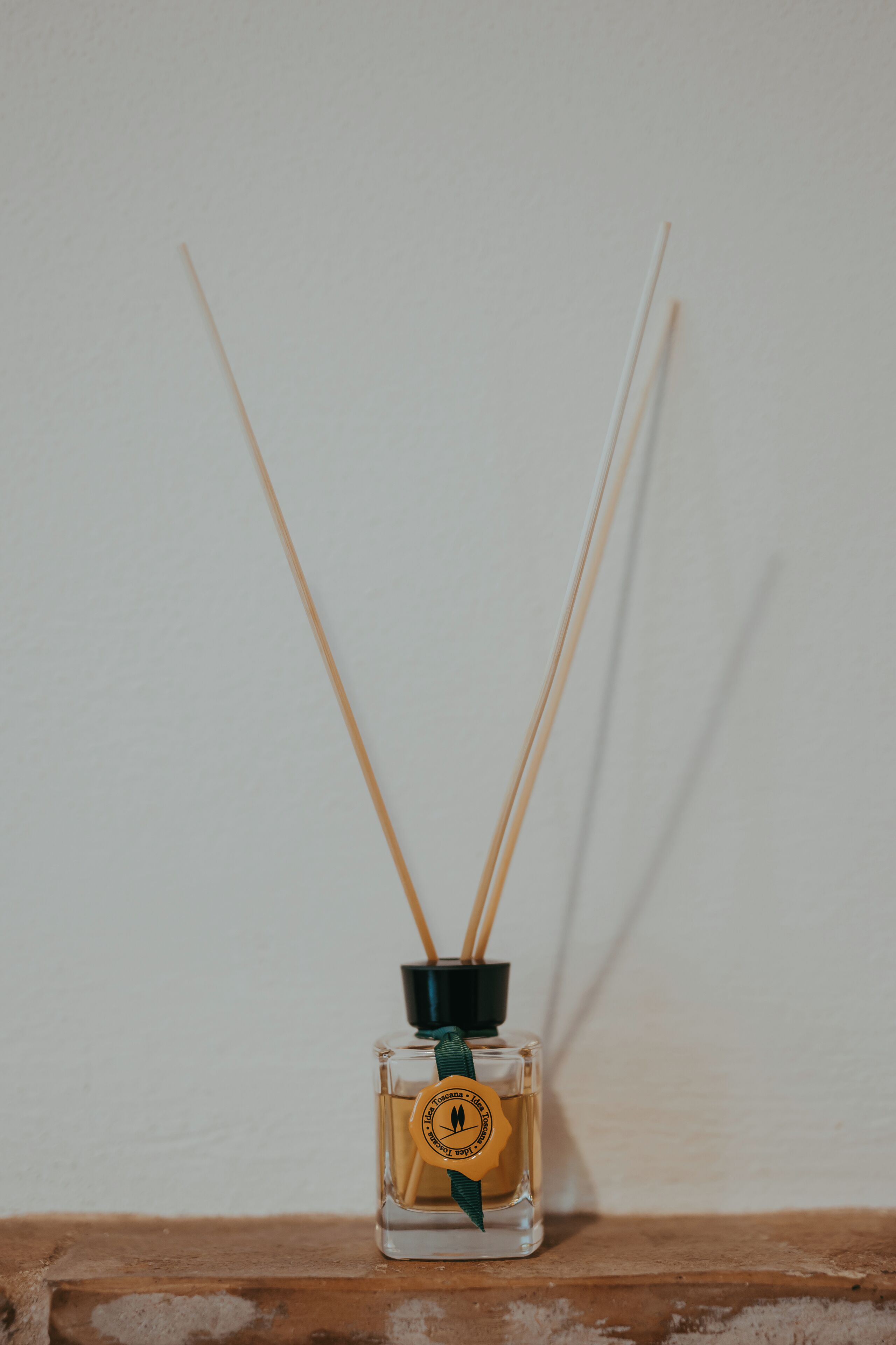 A small glass bottle with a green ribbon and a yellow label, placed on a wooden surface against a plain wall.
