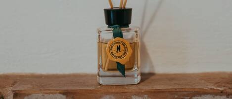 A small glass bottle with a green ribbon and a yellow label, placed on a wooden surface against a plain wall.