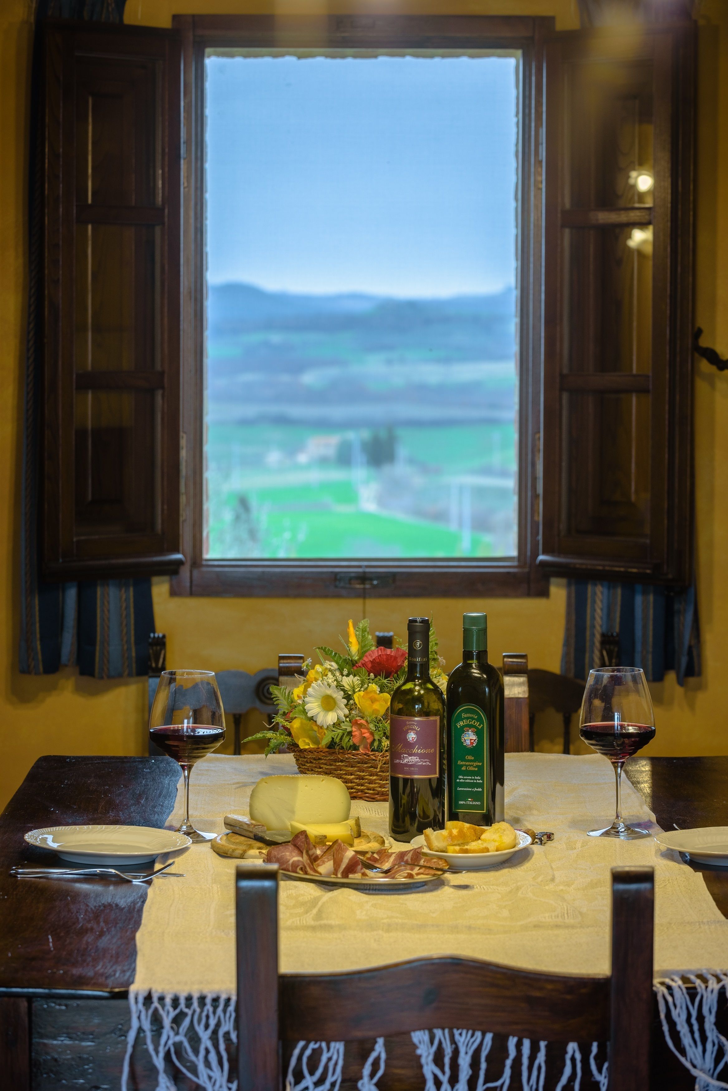 A dining table set with plates, glasses, and bottles, with a window view of a green landscape.