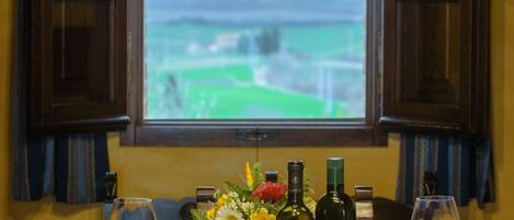 A dining table set with plates, glasses, and bottles, with a window view of a green landscape.