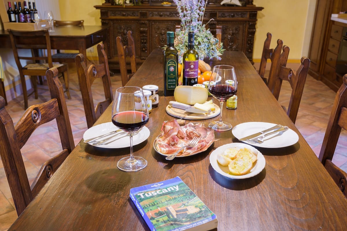 A wooden dining table set with plates, glasses, a book, and food items.
